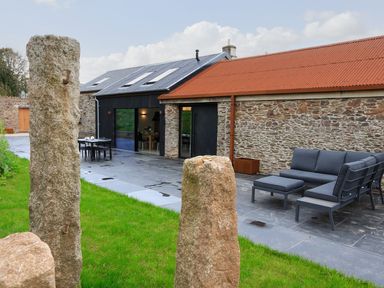 An outdoor patio with stone pillars and slate flooring next to a stone building with a red roof and outdoor seating at The Barns @ Downton in Dittisham