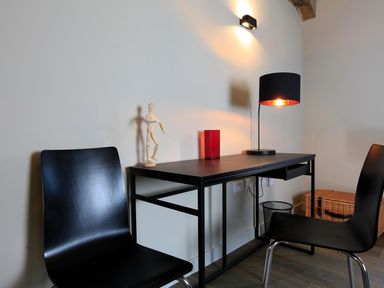 A black desk with a lamp a wooden mannequin and a red object between two black chairs at The Barns @ Downton in Dittisham