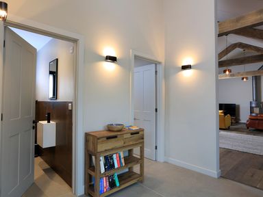 A hallway with a wooden console table with books and a bowl with doors leading to a bathroom and a living room at The Barns @ Downton in Dittisham