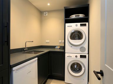 A laundry room with a sink a washing machine and dryer stacked and a fridge at The Barns @ Downton in Dittisham
