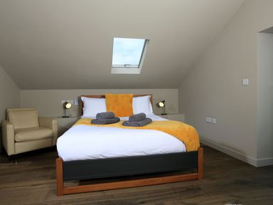 A bedroom with a bed featuring yellow and white bedding and two rolled towels with armchair under a skylight at The Barns @ Downton in Dittisham