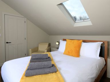 A bedroom with a bed that has white sheets a yellow pillow and gray towels a beige armchair and a skylight window at The Barns @ Downton in Dittisham