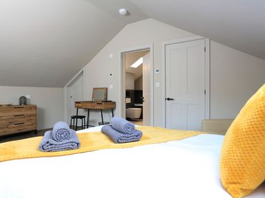 A bedroom with a bed with towels and a yellow throw cushion a wooden dresser and a dressing table at The Barns @ Downton in Dittisham