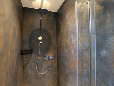 A shower area with dark textured walls a rainfall shower head and a handheld shower at The Barns @ Downton in Dittisham