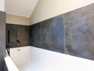 A white bathtub with dark textured tiles on the wall and a black faucet at The Barns @ Downton in Dittisham