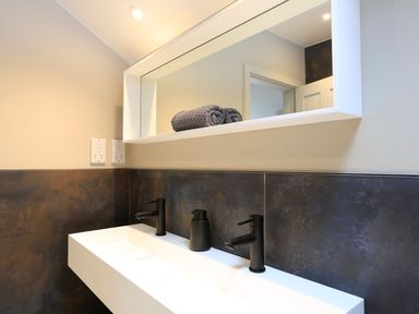 A bathroom sink with two black faucets and a soap dispenser under a rectangular mirror with gray towels on top at The Barns @ Downton in Dittisham