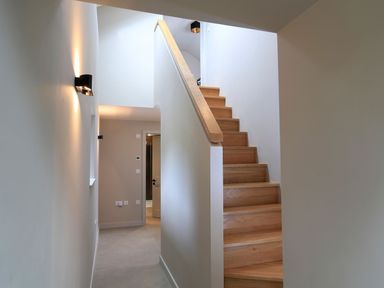 A hallway with wooden stairs and wall lights at The Barns @ Downton in Dittisham