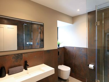 A bathroom with a white sink, wall-mounted toilet, glass shower enclosure, and a small plant near the window at The Barns @ Downton in Dittisham