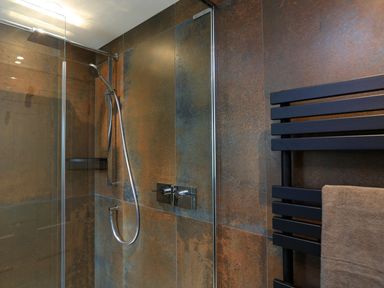 A shower area with a handheld showerhead and a black towel rail with a towel at The Barns @ Downton in Dittisham
