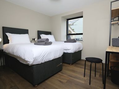 A bedroom with two single beds bedside lamps a window a stool and a desk at The Barns @ Downton in Dittisham