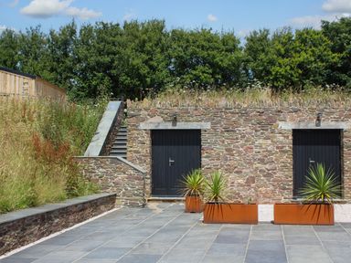 A stone wall with two doors and stairs next to a tiled patio with three rectangular planters at The Barns @ Downton in Dittisham