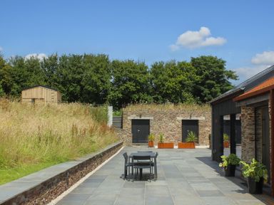 An outdoor patio with a table and chairs and potted plants next to a building and stone wall at The Barns @ Downton in Dittisham