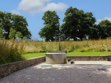 An outdoor hot tub on a gravel area with grass and trees in the background at The Barns @ Downton in Dittisham