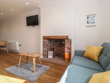 A living room with a blue sofa and yellow cushions a wooden coffee table on a rug a stone fireplace a wall mounted tv and a map hanging at 2 South Street in Fletchertown near Aspatria