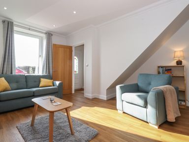 A living room with blue seating a wooden coffee table and a bookshelf with a lamp at 2 South Street Fletchertown near Aspatria