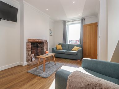 A living room with a blue sofa a wooden coffee table and a stone fireplace at 2 South Street in Fletchertown near Aspatria