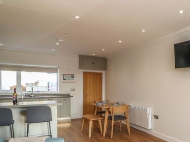 A kitchen and dining area with a wooden dining table set near a wall radiator and a mounted television at 2 South Street in Fletchertown near Aspatria