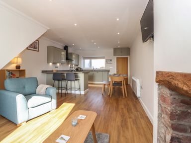 An open plan living area with a blue armchair kitchen island with two stools dining table with chairs and a wall mounted television at 2 South Street in Fletchertown near Aspatria