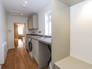 A narrow kitchen with a washing machine sink countertop and wooden floor at 2 South Street in Fletchertown near Aspatria