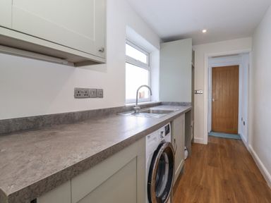 A kitchen with countertop sink washing machine cabinet and wooden door at 2 South Street in Fletchertown near Aspatria