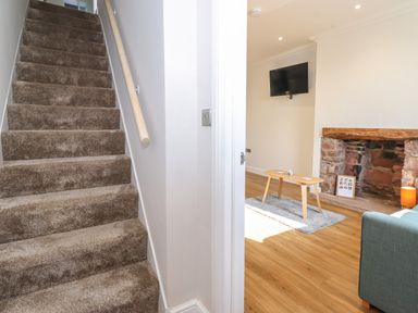 A carpeted staircase next to a living room with a mounted television and a small wooden table on a rug at 2 South Street in Fletchertown near Aspatria