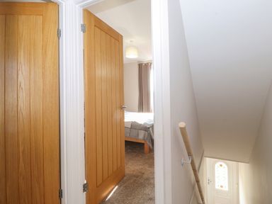 A hallway with two wooden doors one leading to a bedroom and stairs with a handrail and a white door with a stained glass window at 2 South Street in Fletchertown near Aspatria