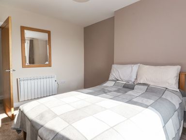 A bedroom with a bed a checkered blanket two pillows a wall mirror an open door and a radiator at 2 South Street in Fletchertown near Aspatria