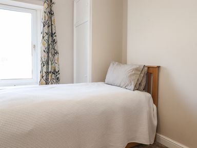 A bedroom with a single bed with white bedding and two pillows near a window with floral curtains at 2 South Street in Fletchertown near Aspatria