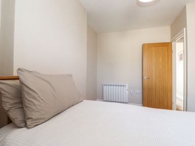 A bedroom with a bed with pillows near a wooden door and a wall-mounted heater at 2 South Street in Fletchertown near Aspatria