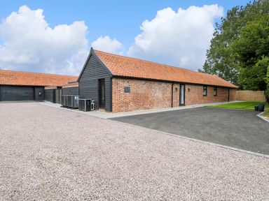A brick and black wooden building with a tiled roof next to gravel and paved driveway at County Farm Barn in South Walsham