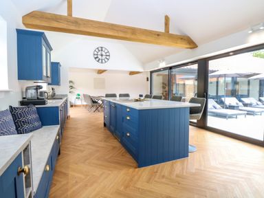 A kitchen with blue cabinets and island a dining area and sliding glass doors to an outdoor seating area at County Farm Barn in South Walsham