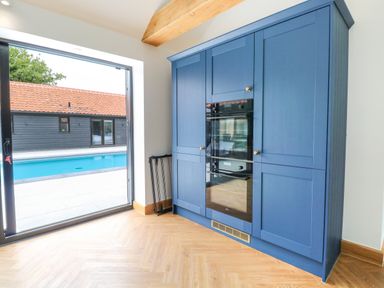 A kitchen area with blue cabinets and built-in ovens next to a glass door overlooking a swimming pool at County Farm Barn in South Walsham