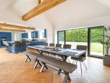 A dining area with a table seating eight and a kitchen with blue cabinets and stools at County Farm Barn in South Walsham