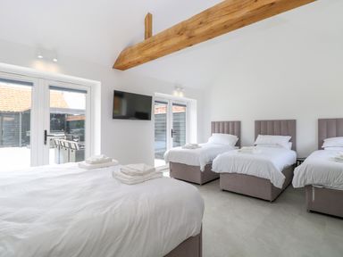 A bedroom with four beds a television mounted on the wall and glass doors leading outside at County Farm Barn in South Walsham