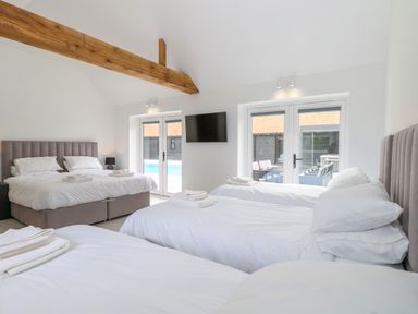 A bedroom with three beds a wall mounted TV wooden ceiling beams and glass doors at County Farm Barn in South Walsham