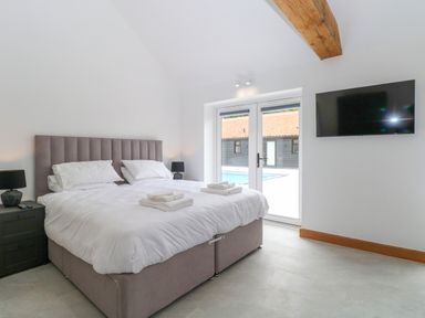 A bedroom with a double bed two bedside tables black lamps a wall-mounted TV and double doors leading outside at County Farm Barn in South Walsham