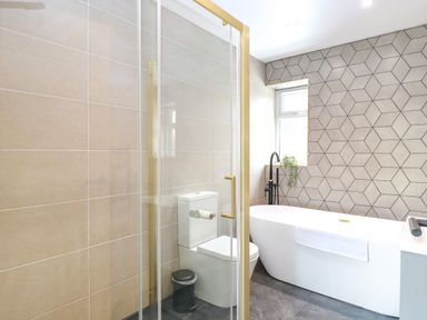 A bathroom with a shower enclosure toilet and freestanding bathtub by a window with patterned wall tiles at County Farm Barn South Walsham