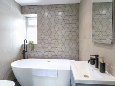 A bathroom with a white bathtub a sink with black faucet and soap dispenser and geometric patterned tiled wall at County Farm Barn in South Walsham
