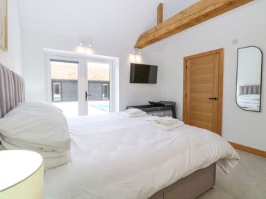 A bedroom with a bed and pillows a wooden door a wall mounted TV and a mirror at County Farm Barn South Walsham