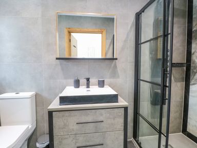 A bathroom with a toilet a sink vanity with two containers a mirror above and a glass shower enclosure at County Farm Barn in South Walsham