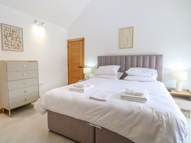 A bedroom with a large bed with white linens towels on top bedside tables with lamps and a chest of drawers at County Farm Barn South Walsham