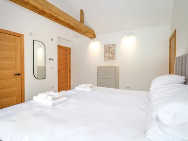 A bedroom with a large bed with white linens wooden doors a tall chest of drawers and a wall mirror at County Farm Barn South Walsham
