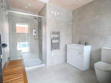 A bathroom with a glass shower enclosure a white vanity with a sink a toilet and a wooden bench at County Farm Barn in South Walsham