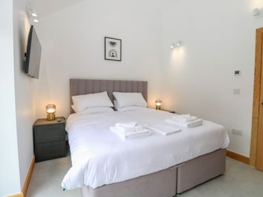 A bedroom with a double bed nightstands lamps a wall-mounted television and a framed picture at County Farm Barn in South Walsham