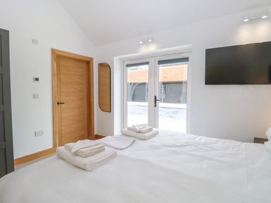A bedroom with a bed with folded towels on it a wooden door a wall-mounted tv and glass doors leading outside at County Farm Barn in South Walsham