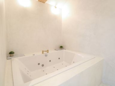 A bathroom with a built-in white jacuzzi tub and two small potted plants on marble slabs at County Farm Barn in South Walsham