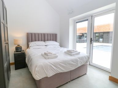 A bedroom with a bed towels on it a bedside table with a lamp and a wardrobe next to glass doors at County Farm Barn in South Walsham