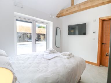 A bedroom with a bed and folded towels by a glass door a wall-mounted TV and a wooden door at County Farm Barn in South Walsham