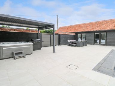 A patio with a hot tub barbecue dining table and chairs outside a building with black walls and a red tiled roof at County Farm Barn in South Walsham