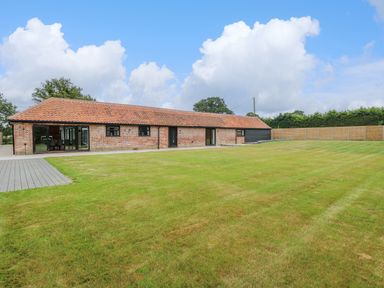 A long brick building with a tiled roof and large grassy lawn at County Farm Barn in South Walsham